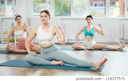 Young girls doing arm workout with band sitting leg extended Young girls doing arm workout with band sitting leg extended 118377571