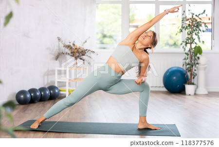 Young woman yoga trainer performing extended side angle pose on black rug 118377576