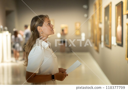 Woman with sheet piece of paper in hands view pictures and icons in museum hall Woman with sheet piece of paper in hands view pictures and icons in museum hall 118377709