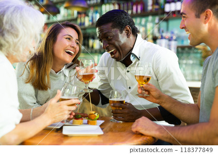 Company of multiracial friends drinking beer and talking with each other during the rest in a pub Company of multiracial friends drinking beer and talking with each other during the rest in a pub 118377849