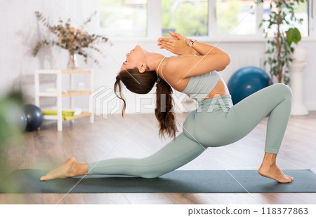 Young woman yoga trainer performing crescent lunge pose on black rug Young woman yoga trainer performing crescent lunge pose on black rug 118377863