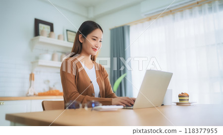 Beautiful young Asian woman working with laptop computer in home kitchen. Work at home 118377955