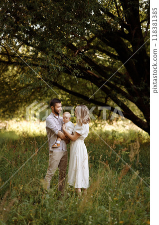 A family of three, a man and a woman with a child in their arms, stand in a park in the summer.  118381385