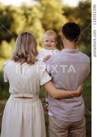 A family of three, a man and a woman with a child in their arms, stand in a park in the summer. A family of three, a man and a woman with a child in their arms, stand in a park in the summer. 118381386