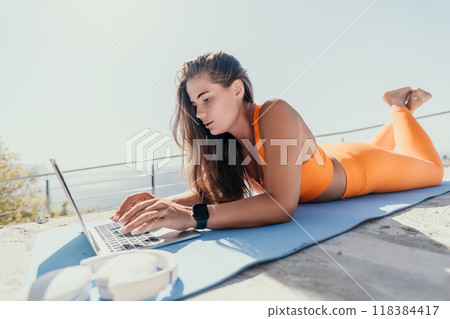 Woman in Orange Sportswear Working on a Laptop Outdoors Woman in Orange Sportswear Working on a Laptop Outdoors 118384417