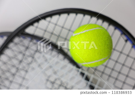 A yellow tennis ball lies against the background of two tennis rackets lying on top of each other on a white background in close-up. Concept of sports and competitions. High quality photo 118386933