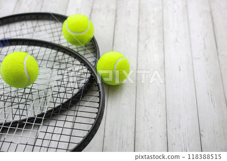 Two tennis rackets lie on top of each other on the left of the photo, yellow tennis balls against a white tree background lie on them and next to them. High quality photo Two tennis rackets lie on top of each other on the left of the photo, yellow tennis balls against a white tree background lie on them and next to them. High quality photo 118388515