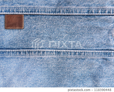 Blue denim texture with a seam and old leather label. Light blue color denim jeans material and vintage tag of brown color. Mock up template. Copy space for text 118390448