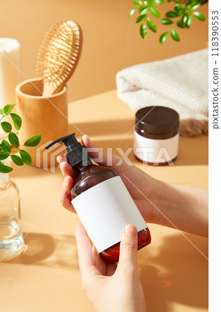 A model holds a brown bottle with white label and black pump dispenser, promoting spa and beauty care products, surrounded by hairbrush, towel, and plant. 118390553