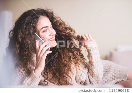 Beautiful young woman lying on bed, making phone call on smartphone, smiling. 118390618