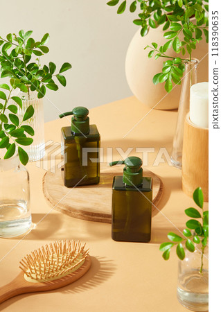 Minimal beige backdrop features two square green bottles with pumps are on a wooden plate with small green plants, a white candle and a wooden brush are on the table. Template for beauty care ads. Minimal beige backdrop features two square green bottles with pumps are on a wooden plate with small green plants, a white candle and a wooden brush are on the table. Template for beauty care ads. 118390635