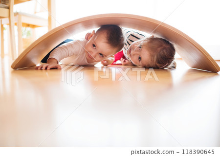 Siblings are playing together in the living room, lying under a wooden arch. 118390645