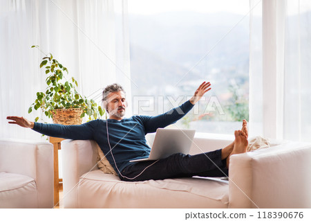 Man at home sitting on sofa with laptop on knees, headphones on head, listening meditating music. 118390676