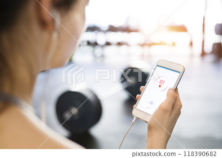 Young fitness girl checking her performance on smatphone after hard workout in gym. Young fitness girl checking her performance on smatphone after hard workout in gym. 118390682