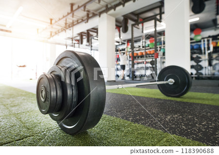 Barbell on gym floor. Rows of gym equipment, metal barbells, dubbells on racks for strength training in gym. 118390688