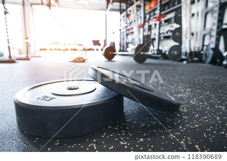 Weight plates on gym floor. Rows of gym equipment, metal barbells, dubbells on racks for strength training in gym. 118390689