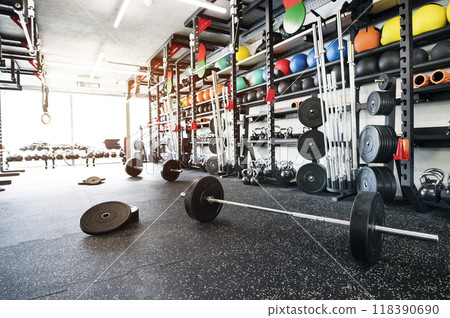 Barbell on gym floor. Rows of gym equipment, metal barbells, dubbells on racks for strength training in gym. Barbell on gym floor. Rows of gym equipment, metal barbells, dubbells on racks for strength training in gym. 118390690