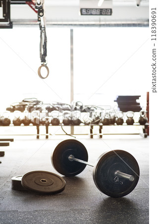 Barbell on gym floor. Rows of gym equipment, metal barbells, dubbells on racks for strength training in gym. 118390691