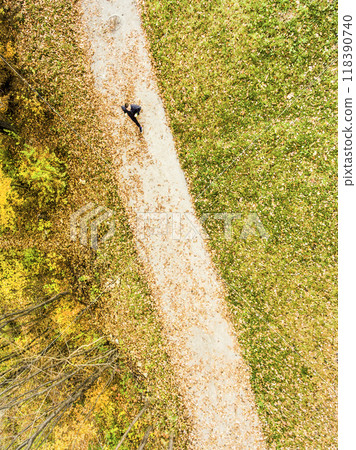 Aerial view of a runner running through autumn park on jogging path with fallen leaves. Morning running training. Aerial view of a runner running through autumn park on jogging path with fallen leaves. Morning running training. 118390740