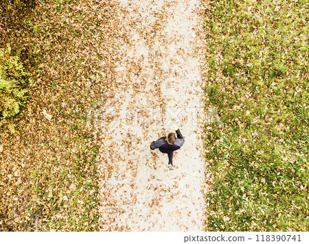 Aerial view of a runner running through autumn park on jogging path with fallen leaves. Morning running training. Aerial view of a runner running through autumn park on jogging path with fallen leaves. Morning running training. 118390741