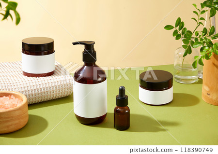 Beauty products advertising template showcases four amber glass beauty products, salt bowl, white towel, and green leaves, surrounded by a yellow wall background and a glass vase with green foliage Beauty products advertising template showcases four amber glass beauty products, salt bowl, white towel, and green leaves, surrounded by a yellow wall background and a glass vase with green foliage 118390749