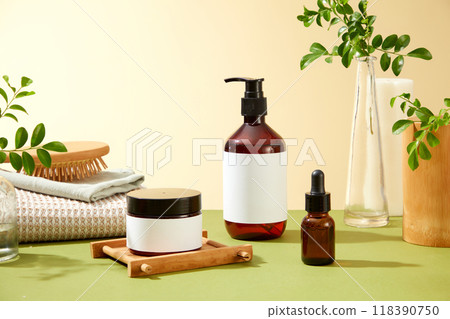 A green surface features a collection of brown glass bottles, a jar, a wooden tray, a white towel, a bamboo hair brush, and a vase with green branches for spa or beauty product advertising. A green surface features a collection of brown glass bottles, a jar, a wooden tray, a white towel, a bamboo hair brush, and a vase with green branches for spa or beauty product advertising. 118390750