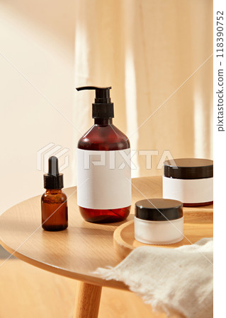 A wooden table displays a collection of beauty products, including a brown glass pump bottle, dropper bottle, and cream jar, with a white label for branding, perfect for beauty product advertising. 118390752