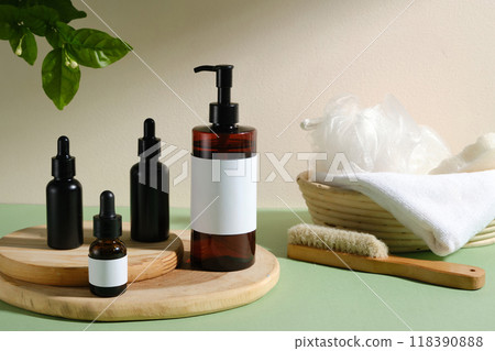 The image depicts a spa-like atmosphere with brown glass bottles, white labels, a large pump bottle, cream jar, white towel, wooden hair comb, and wicker basket. Promoting spa or beauty products. 118390888