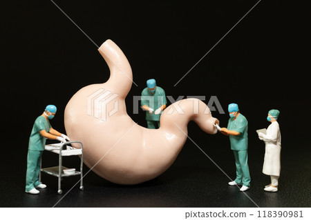 Miniature surgeons in scrubs performing an operation on a large model of a human stomach. Miniature surgeons in scrubs performing an operation on a large model of a human stomach. 118390981