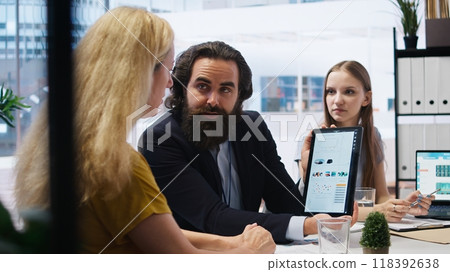 Financial advisor showing statistical graphs on tablet to clients, analyzing market trends to optimize their income. Mother and daughter checking investment plan on device, camera A Financial advisor showing statistical graphs on tablet to clients, analyzing market trends to optimize their income. Mother and daughter checking investment plan on device, camera A 118392638