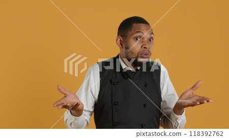 Professional waiter showing clueless sign and being unsure, shrugging and saying i dont know in studio. Confused butler staff in apron feeling uncertain and doubtful about something. Camera A. Professional waiter showing clueless sign and being unsure, shrugging and saying i dont know in studio. Confused butler staff in apron feeling uncertain and doubtful about something. Camera A. 118392762