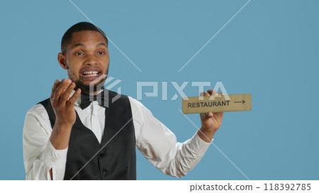 Doorman bellhop showing the restaurant direction with a hotel sign, holding an indicator to point guests to the amenities. Professional hotel concierge using a wall mark. Camera A. 118392785
