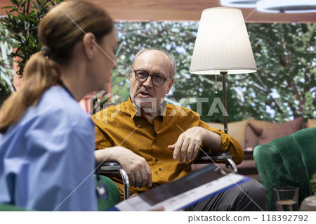 Professional caretaker discussing with old woman in wheelchair and her husband, comforting her patients at home. Nurse consulting elderly people, prescribe medical treatment. 118392792