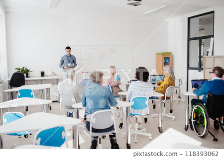 Teacher explaining senior students how to work with laptop and internet. Elderly people attending computer and technology education class. Digital literacy. 118393062
