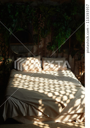 Bed with plain linen, with spots of light from the blinds. Cozy boho style bedroom 118393957