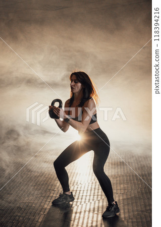 A Dynamic Woman excels in the Kettlebell Workout, inspired by her atmospheric setting that enhances her focus, determination, and commitment to fitness and wellness, boosting her performance 118394216