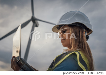 A talented female engineer is actively monitoring wind turbines using her laptop in the dynamic and innovative field of renewable energy, focusing on sustainability and technological advancements 118394298