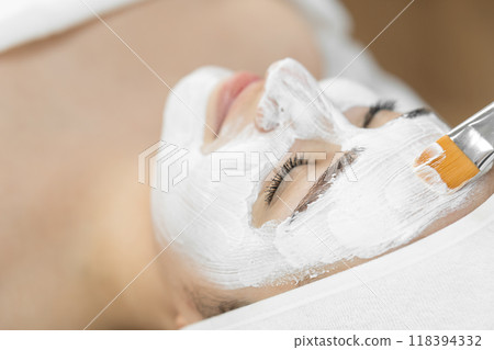 Indulge in a peaceful spa experience with a luxurious facial treatment using a white mask for rejuvenating skincare in a serene setting. Enjoy a moment of relaxation and beauty pampering 118394332