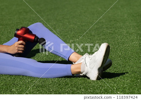 Woman massaging legs with massage percussion gun after training. Applying therapeutic percussion massager gun. 118397424