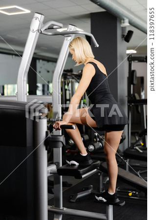Blond athletic woman wearing a black suit doing leg exercises in the gym 118397655