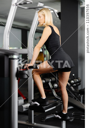 Blond athletic woman wearing a black suit doing leg exercises in the gym Blond athletic woman wearing a black suit doing leg exercises in the gym 118397656