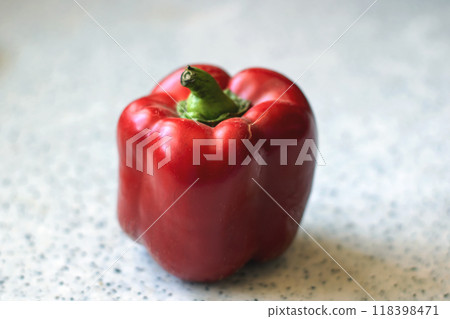 A bright red pepper featuring a green stem is resting on a counter 118398471