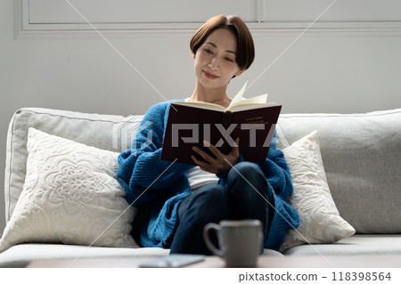 Middle-aged woman reading a book on the sofa Middle-aged woman reading a book on the sofa 118398564