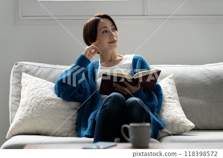 Middle-aged woman reading a book on the sofa Middle-aged woman reading a book on the sofa 118398572