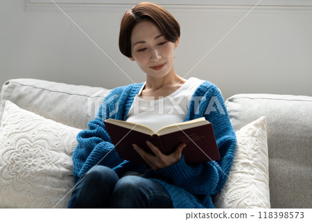 Middle-aged woman reading a book on the sofa Middle-aged woman reading a book on the sofa 118398573
