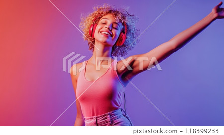 Young woman with short curly blonde hair dancing joyfully against a purple gradient background, wearing red headphones, pink tank top, and high-waisted jeans, radiating vibrant energy. Happiness and 118399233