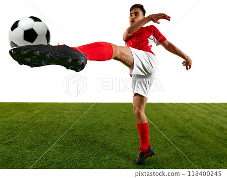 Dynamic shot of football player, dressed in red and white, focuses on powerful kick during training on green field against white background. Game-winning skills. 118400245