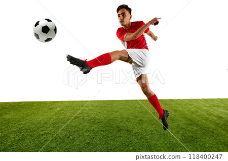 Young athletic man, football player, dressed in red and white uniform, performs high kick, focusing on controlling ball with precision on green field. Young athletic man, football player, dressed in red and white uniform, performs high kick, focusing on controlling ball with precision on green field. 118400247