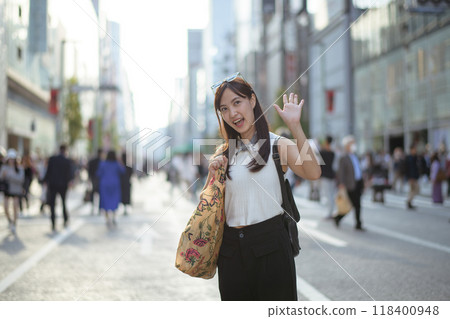 Urban lifestyle in Japan, A young Asian woman with a tote bag, smiling amidst greenery and snowy sidewalks, Copy space for a personalized message. Urban lifestyle in Japan, A young Asian woman with a tote bag, smiling amidst greenery and snowy sidewalks, Copy space for a personalized message. 118400948