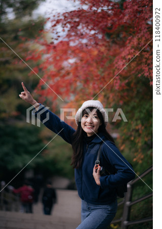 Asian woman in Japan's fall beauty, a cheerful holiday portrait in Kyoto. Vibrant foliage, friends, and smiles by the lake create a joyful and scenic atmosphere. 118400972